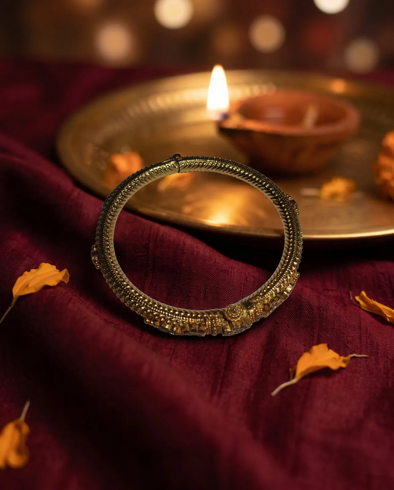 The same carved gold kada on maroon silk with a brass diya plate behind it