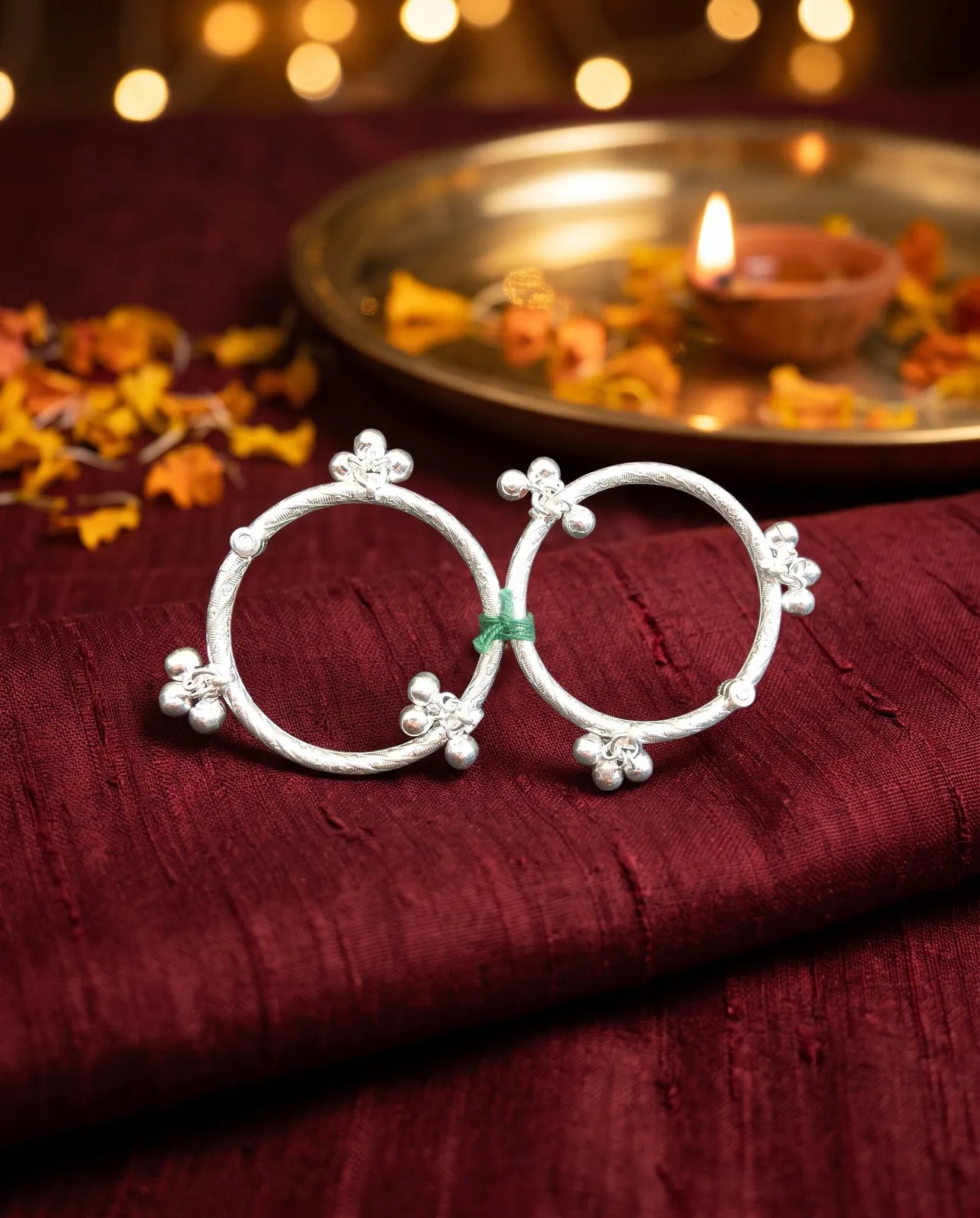 The same silver anklets on maroon silk with a brass diya plate and marigolds